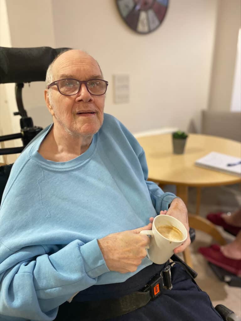 Man in blue sweatshirt in wheelchair holds cup of tea